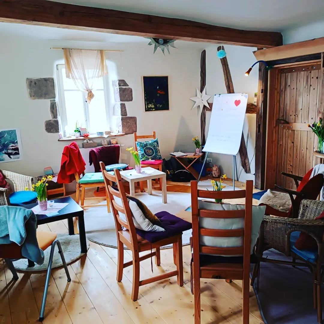 Gemütlicher Workshop-Raum in altem Bauernhaus. Mit Stühlen, Tischen, Flipchart, Blumen.