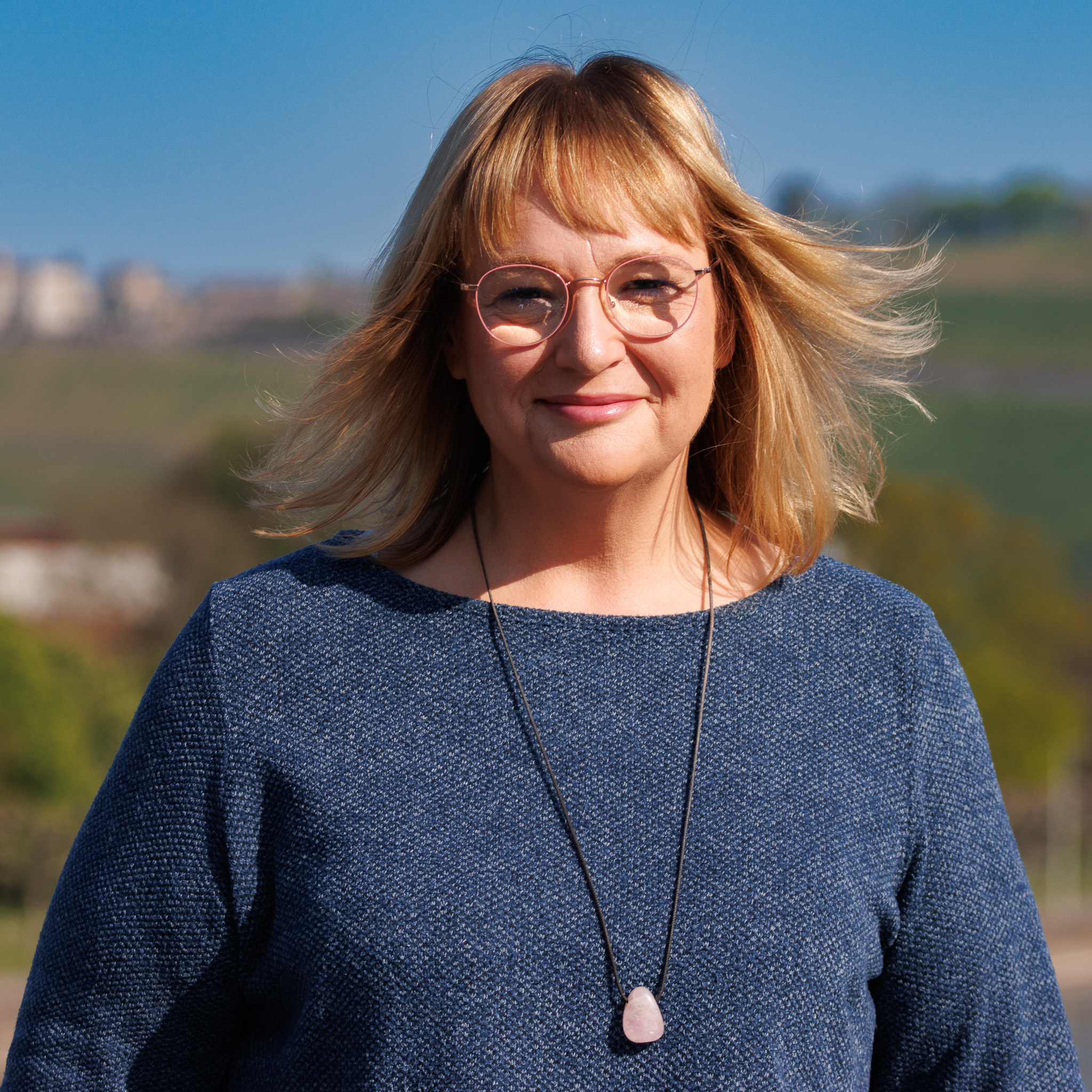 Andrea Dillmaier auf der alten Mainbrücke in Würzburg in blauem Kleid mit Lächeln und wehendem Haar.