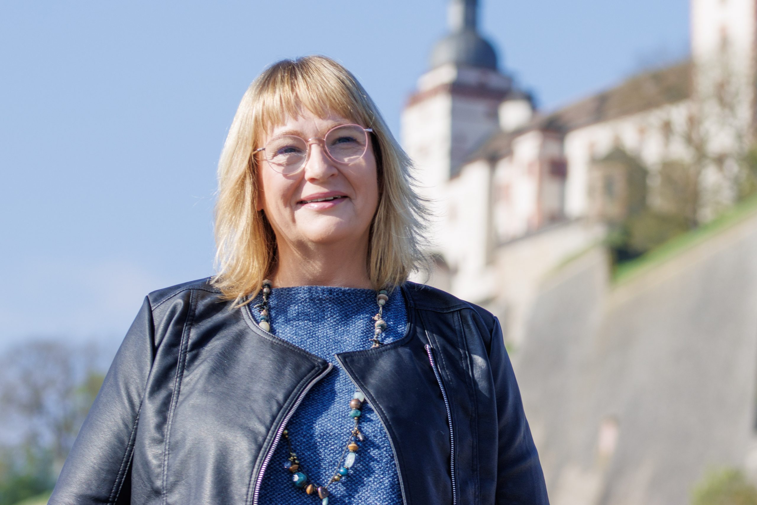 Andrea vor der Festung Marienberg in Würzburg n einer schwarzen Lederjacke.